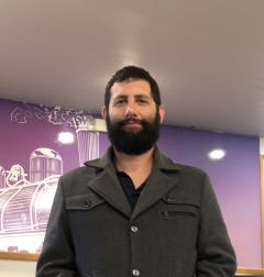 Man with dark hair and full beard with dark jacket